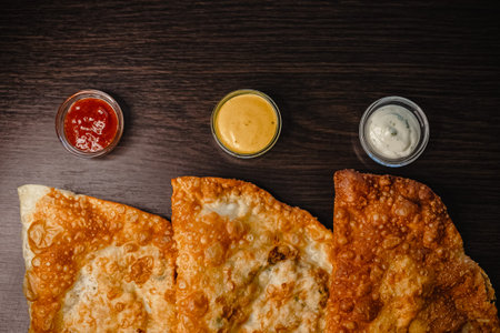 Crispy fried flatbread with three flavorful sauces on dark wooden table.