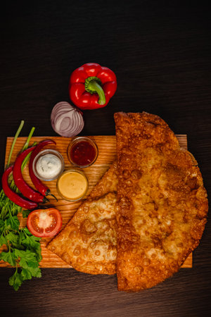 Crispy fried dough pasties with colorful vegetables and sauces on wooden board.の写真素材