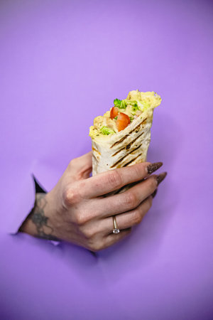 Female hand holding delicious wrap against purple background.の写真素材