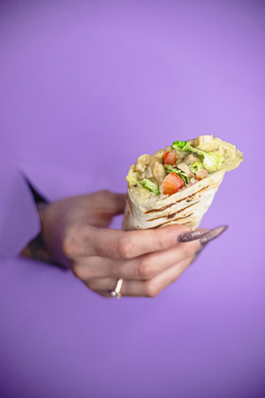 Close-up of female hand holding grilled chicken wrap against purple background.の写真素材