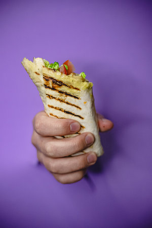 Grilled wrap in hand with vibrant purple background.の写真素材