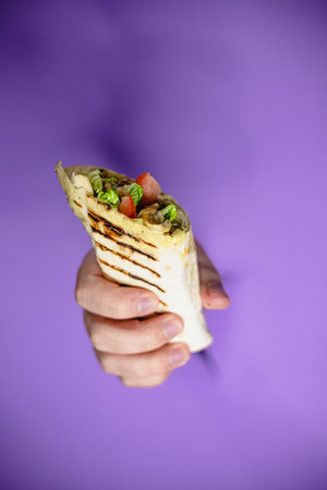 Hand holding freshly grilled wrap against purple background.の写真素材