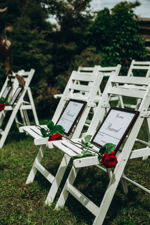 Outdoor wedding ceremony with reserved seating and roses on white chairs.の写真素材