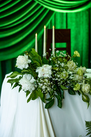 Elegant white floral arrangement on draped table with green backdrop and candles.の写真素材