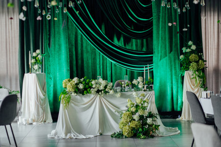Elegant wedding reception decor with green drapes and white floral arrangements.の写真素材