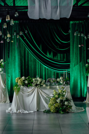 Elegant green and white wedding venue decor with draped backdrop and floral arrangements.の写真素材
