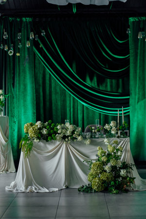 Elegant wedding reception table with floral arrangements and green drapes.の写真素材