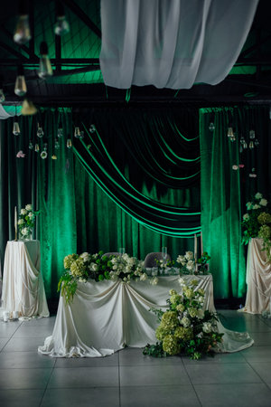 Elegant wedding reception table with floral greenery and draped curtains.の写真素材