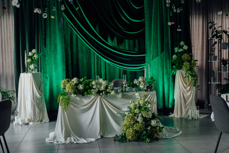 Elegant wedding reception decor with green drapes and white floral arrangements.の写真素材