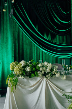 Elegant event table with green floral arrangements and draped curtains.の写真素材