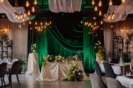 Elegant green and white wedding reception decor with drapes and hanging lights.の写真素材