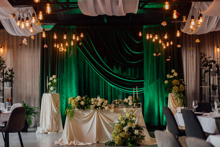 Elegant wedding reception venue with lush green drapes and floral arrangements.の写真素材