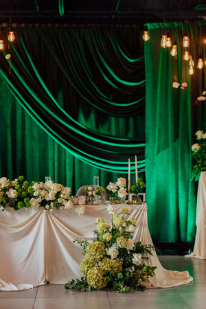 Elegant wedding reception table with floral arrangement and green draped background.の写真素材