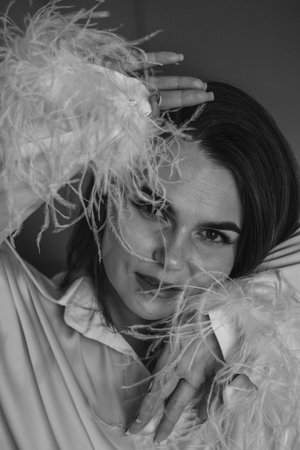 Female caucasian adult in elegant feathered outfit with thoughtful expression.の写真素材