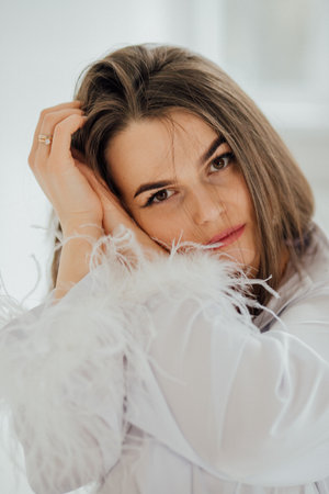 Young caucasian female in feathered white attire posing indoors.の写真素材
