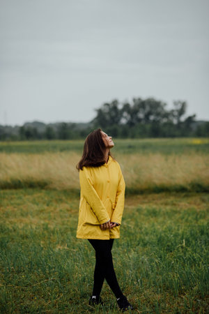 Woman in yellow raincoat enjoys the serene beauty of a rainy day in the countryside.