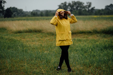 Woman enjoying a rainy day outdoors in a yellow raincoat in the field.の写真素材
