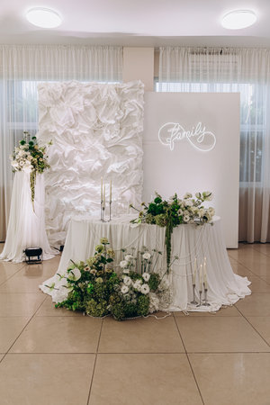 Elegant white and green wedding decor with floral arrangements and a family neon sign backdrop.の写真素材