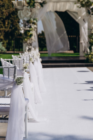 Elegant outdoor wedding ceremony setup with white floral decorations and draped chairs.の写真素材