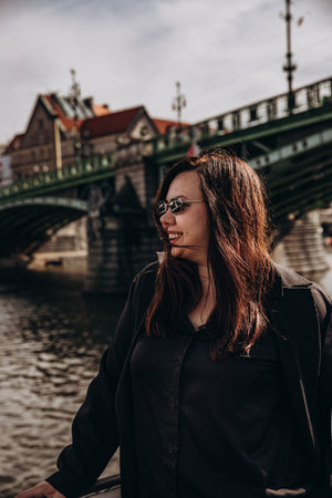 Young woman enjoying a sunny day by the river with an architectural bridge backdrop.の写真素材
