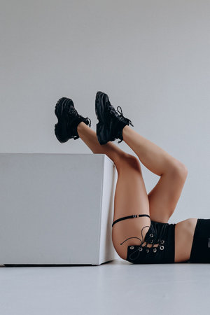 Fashionable woman wearing black boots and shorts posing creatively on a white background.の写真素材