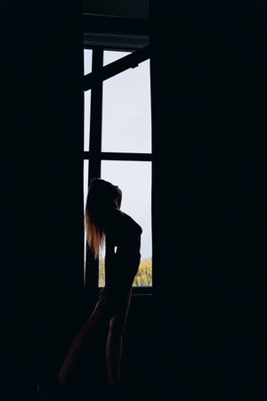 Silhouette of a woman stretching gracefully near a window with a background of natural light.の写真素材