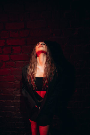 Woman in dramatic red lighting leaning against brick wall.