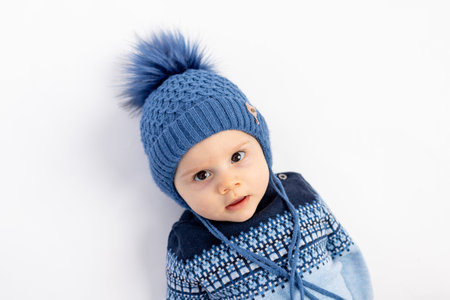 a smiling little boy in a Winter hat with a pompom lies and looks at the camera-a portrait of a...