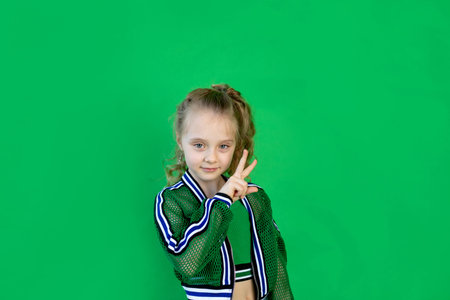 a cheerful girl with curly hair looks at the camera and shows two fingers, standing on a green background. space for textの写真素材