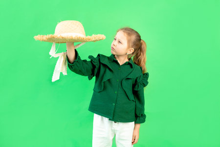 a 6-7-year-old girl on a green isolated background holds a straw hat, a place for textの写真素材