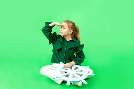 a 6-7-year-old girl on a green isolated background looks into the distance, a place for textの写真素材