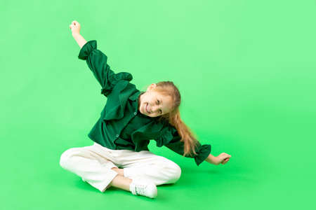 a 6-7-year-old girl on a green isolated background is happy and laughing, hands to the sides, space for textの写真素材