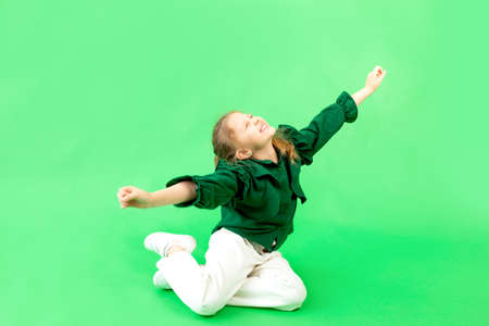 a 6-7-year-old girl on a green isolated background is happy and laughing, hands to the sides, space for textの写真素材
