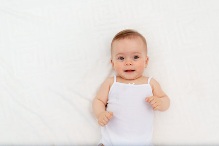 portrait of a smiling baby girl 6 months old lying in a crib in the children's room on her back,...