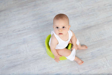 small baby boy 8 months old sitting on a potty, baby toilet, place for textの写真素材