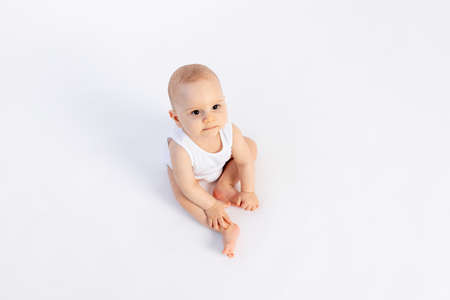 cute baby boy in a white bodysuit on a white isolated background looks at the camera, baby 8 months, children's fashion, advertising children's clothing, space for textの写真素材