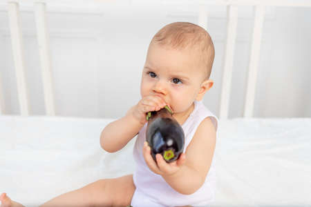 little baby boy 8 months old sitting on the bed in the nursery with vegetables, baby feeding, baby food concept, place for textの写真素材