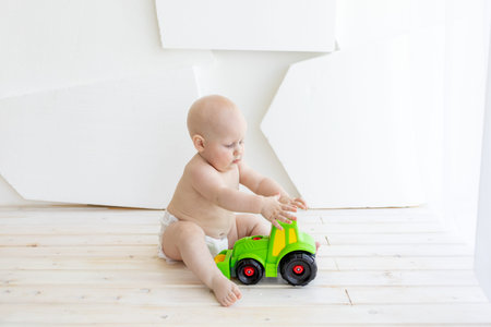 baby boy 8 months old sitting in diapers with a green toy typewriter at the window, a place for text