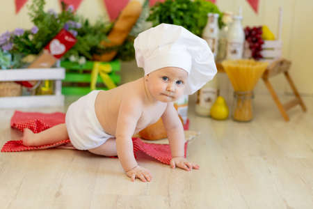 a baby in a cook's hat sits in a beautiful photo zone with flour and vegetables, a baby cook, a child with flour and bread prepares foodの写真素材