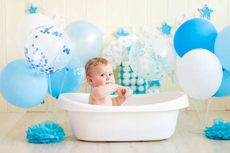 baby boy celebrates birthday 1 year in a bath with balloons, bathing baby with blue balloonsの写真素材