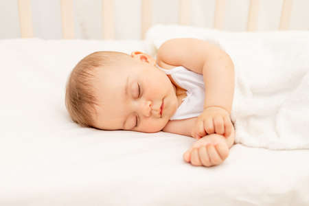 Small baby girl 6 months old sleeping in a white bed, healthy baby sleepの写真素材