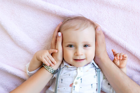 a small baby boy 1 year old lies on the bed, dad hugs the baby's head, the concept of a happy...