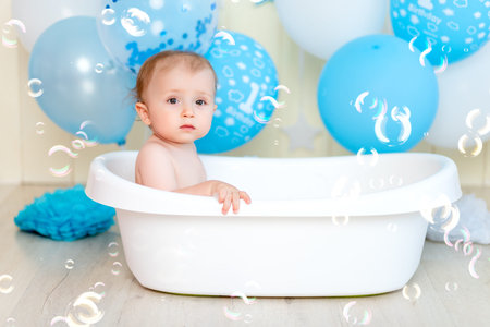 baby boy bathes in a bathtub with balloons and soap bubbles, happy childhood, children's birthday.