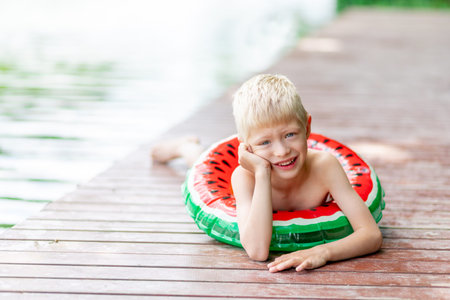 a blond boy lies on a pier near a lake with a circle in the summer, a child's rest in the village