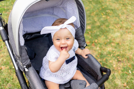 a small child a girl of 7 months sits in a stroller in the summer in a white dress and laughs