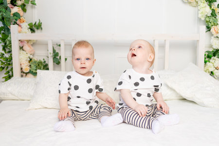 two baby twins 8 months old sitting on the bed in the same clothes, brother-sister relationship,...