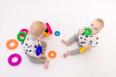 two twin babies 8 months old play on a white isolated background, early development of children up to a year old, a child takes a toy from another, a place for textの写真素材