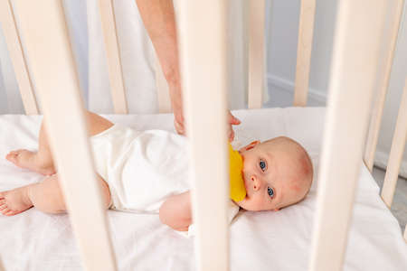 baby 6 months old girl lying in the crib, morning baby, baby put to bed, little baby looks through the crib into the camera, place for textの写真素材