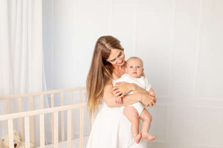 young beautiful mother holding her daughter 6 months in the nursery standing by the crib, mother's day, place for textの写真素材