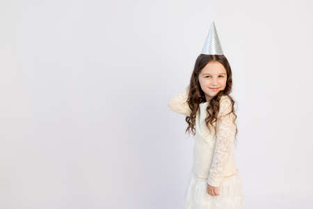 A cute little girl with a cap on a white isolated background is dancing and rejoicing. Space for text. Little girl celebrates birthday, holiday conceptの写真素材